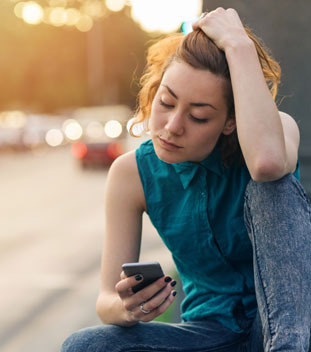 young female with her hand scrunching her hair and looking through her phone for help for cancer patients young female with her hand scrunching her hair and looking through her phone for help for cancer patients