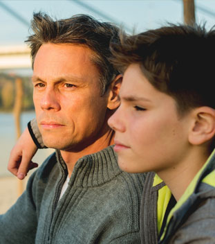 young son with his arm over his dad wearing a grey jumper. image for family support for cancer patients & family cancer young son with his arm over his dad wearing a grey jumper. image for family support for cancer patients & family cancer