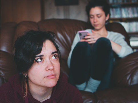 young person on the couch looking at her phone and another young person sitting down in front of the couch. family cancer young person on the couch looking at her phone and another young person sitting down in front of the couch. family cancer